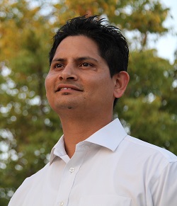A photo of Anand shoulders up with trees in the background