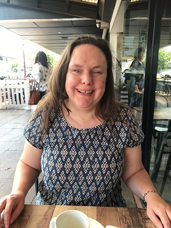 A front on photo of Jess sitting at a table smiling at the person taking the photo